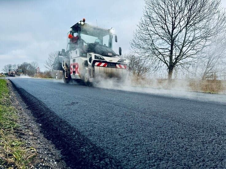 Mehrere Walzen bringen die neue Asphaltdeckschicht in Form: Die Sanierung der L 4 in Brookmerland nähert sich dem Ende